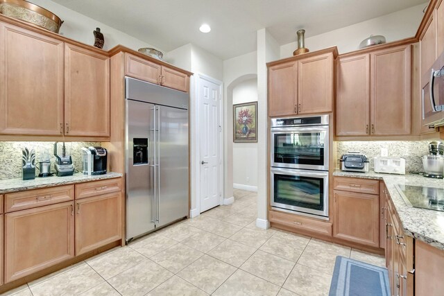 16211 Rosecroft Ter, Delray Beach, FL 33446 - kitchen featuring decorative backsplash, appliances with stainless steel finishes, arched walkways, light tile patterned floors, and light stone counters