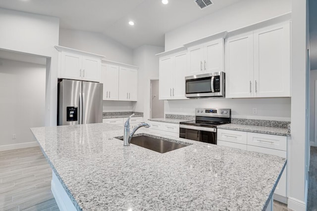 kitchen featuring a sink, stainless steel appliances, visible vents, white cabinets, and an island with sink
