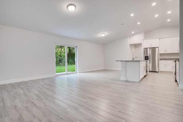 interior space with light wood finished floors, stainless steel refrigerator with ice dispenser, open floor plan, and a center island with sink