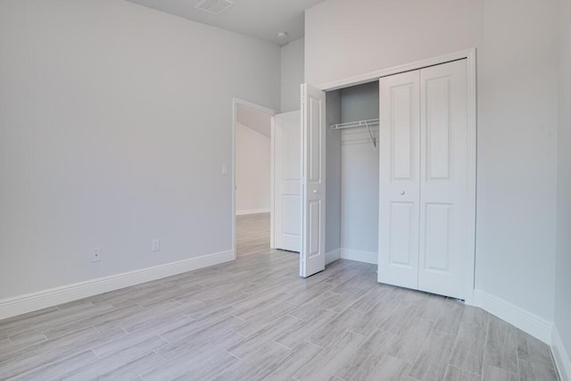 unfurnished bedroom featuring light wood-style floors, baseboards, visible vents, and a closet