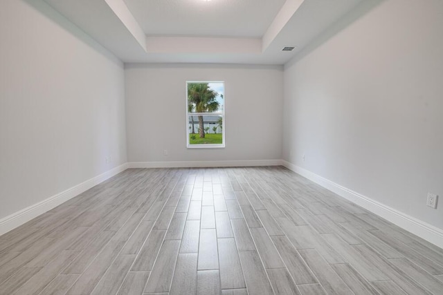 spare room featuring visible vents, light wood-type flooring, a tray ceiling, and baseboards