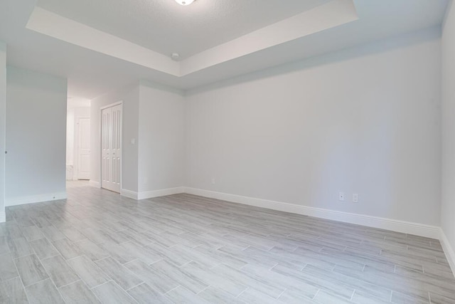 unfurnished room featuring light wood-type flooring, a raised ceiling, and baseboards