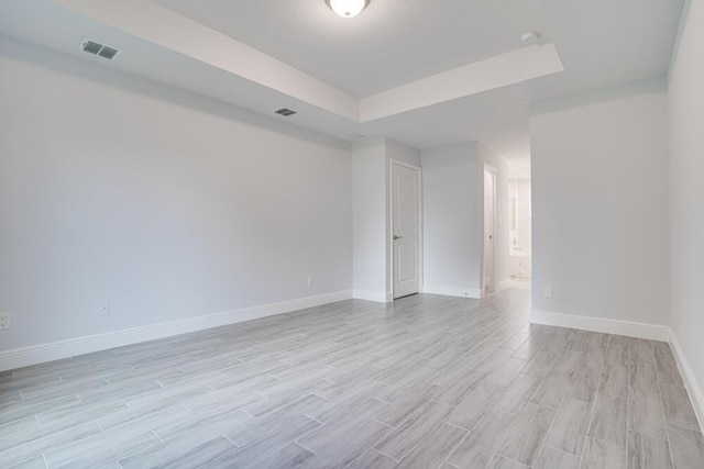spare room with visible vents, a raised ceiling, light wood finished floors, and baseboards