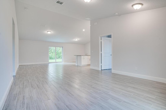 spare room with baseboards, visible vents, light wood-style flooring, and vaulted ceiling