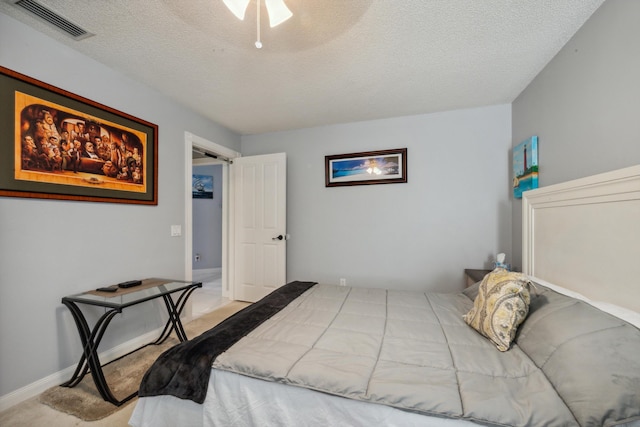 bedroom featuring baseboards, light carpet, a textured ceiling, and visible vents