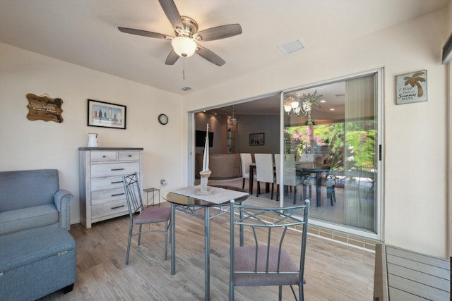 dining space with visible vents, wood finished floors, and ceiling fan with notable chandelier