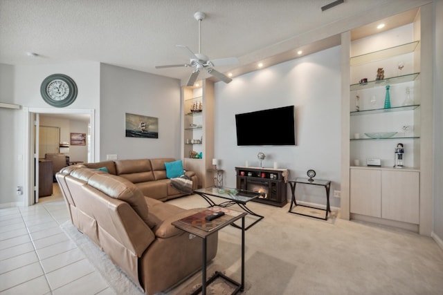 living area with a ceiling fan, a textured ceiling, built in shelves, and light carpet