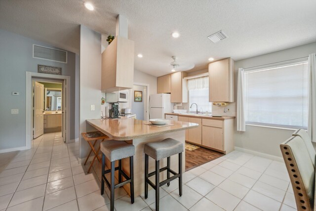 kitchen with visible vents, light brown cabinets, white appliances, a kitchen bar, and a sink