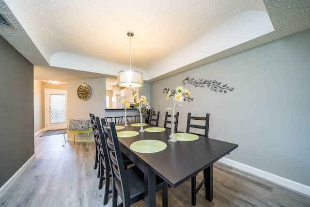 dining room featuring baseboards, a textured ceiling, wood finished floors, and a tray ceiling