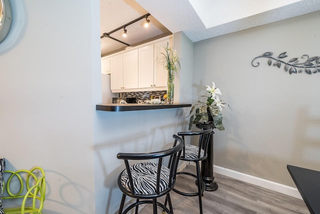 bar featuring track lighting, baseboards, wood finished floors, tasteful backsplash, and a skylight