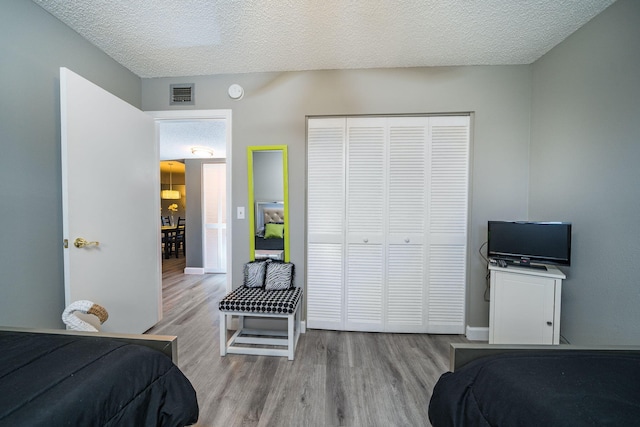 bedroom featuring a textured ceiling, a closet, wood finished floors, and visible vents