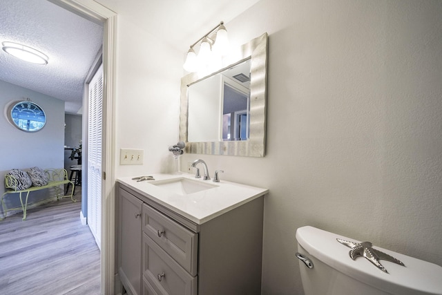 half bath with toilet, a textured ceiling, wood finished floors, and vanity