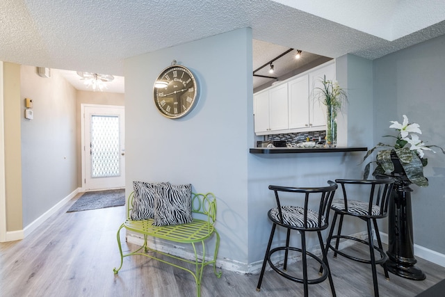 interior space with a textured ceiling, baseboards, rail lighting, and wood finished floors