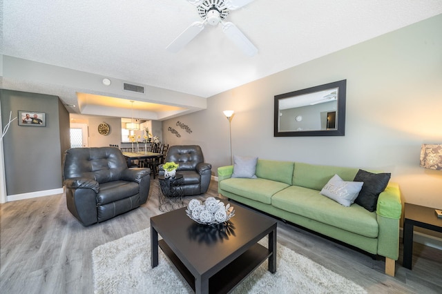 living room featuring visible vents, a ceiling fan, baseboards, and wood finished floors