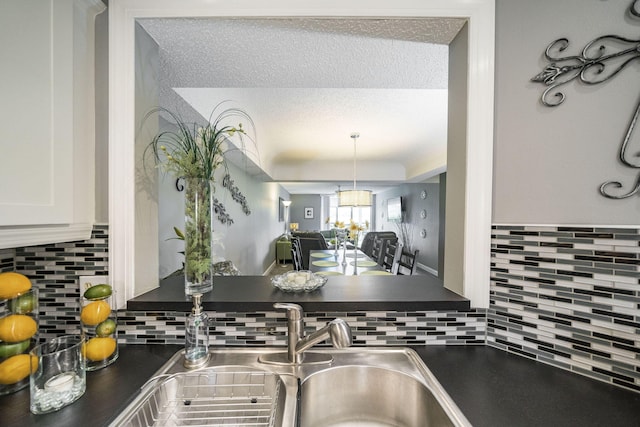 kitchen featuring dark countertops, backsplash, white cabinetry, and a notable chandelier