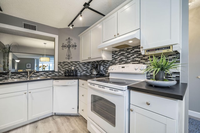 kitchen featuring visible vents, dark countertops, a sink, under cabinet range hood, and white appliances