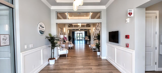 corridor with wood finished floors, a wainscoted wall, and crown molding