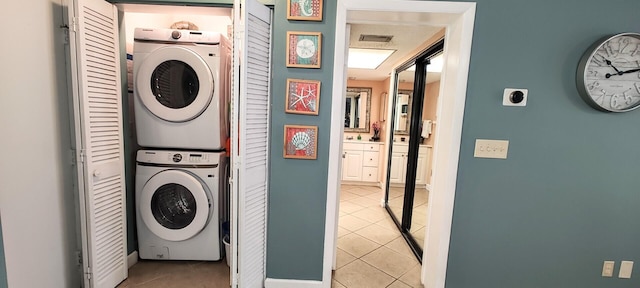 washroom featuring stacked washing maching and dryer, light tile patterned floors, laundry area, visible vents, and baseboards