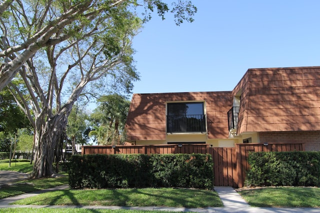 404 Live Oak Ln, Boynton Beach, FL 33436 - view of front of property with fence, a balcony, mansard roof, brick siding, and a front lawn
