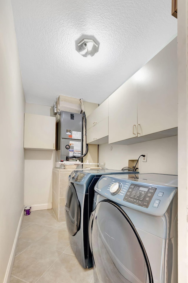 laundry room with a textured ceiling, independent washer and dryer, cabinet space, light tile patterned floors, and baseboards