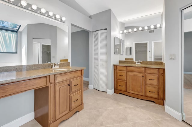 bathroom featuring a sink, two vanities, tile patterned floors, and a skylight