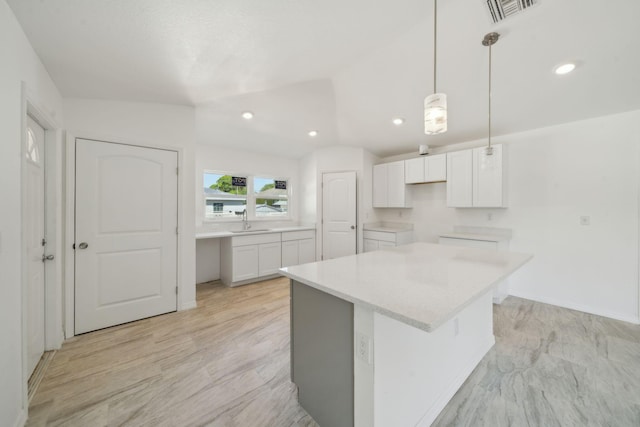 kitchen with hanging light fixtures, a kitchen island, a sink, white cabinetry, and visible vents