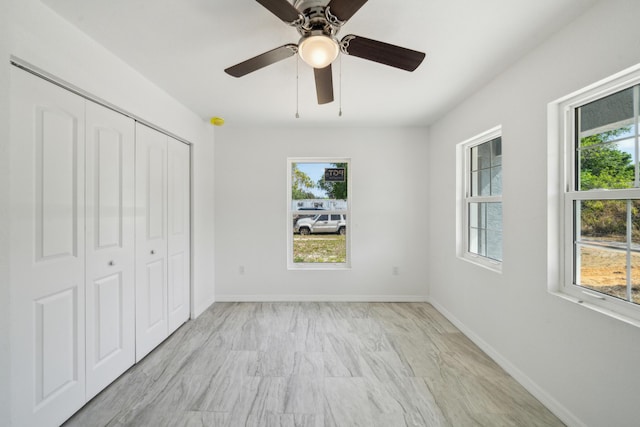 unfurnished bedroom with a closet, multiple windows, ceiling fan, and baseboards