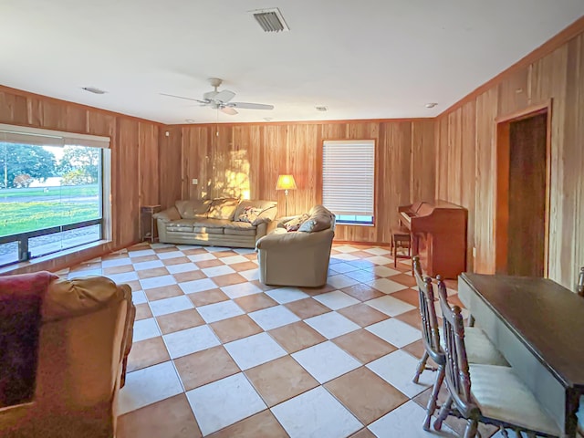 living room with wooden walls, a ceiling fan, and visible vents