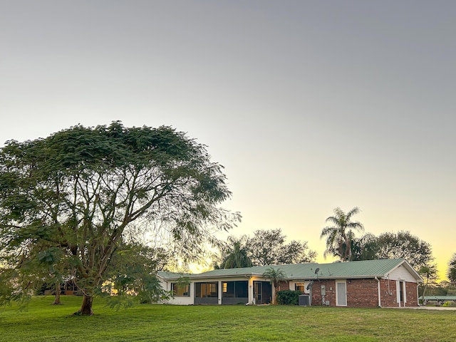 view of front of property with brick siding, metal roof, a sunroom, cooling unit, and a lawn