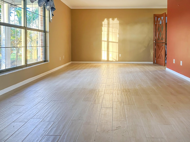 empty room featuring a healthy amount of sunlight, light wood-type flooring, crown molding, and baseboards