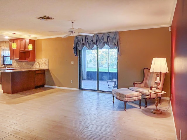 living area featuring crown molding, light wood-type flooring, visible vents, and baseboards