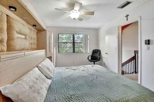 bedroom with a textured ceiling, visible vents, and ceiling fan
