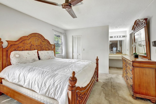 bedroom with a textured ceiling, light colored carpet, ensuite bathroom, a closet, and a ceiling fan