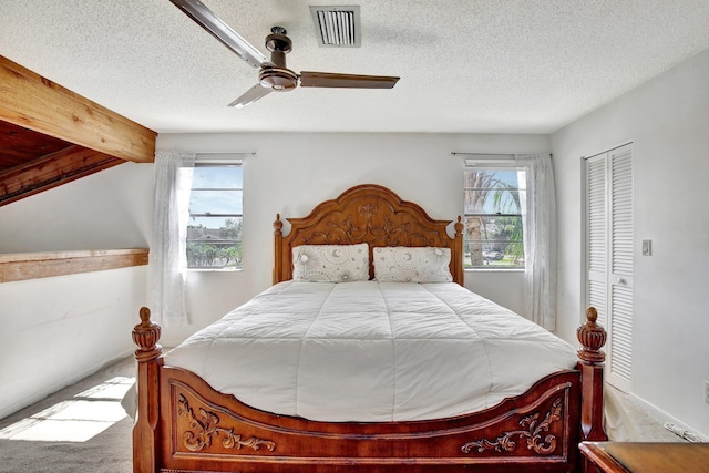 carpeted bedroom with a textured ceiling, visible vents, a ceiling fan, and a closet