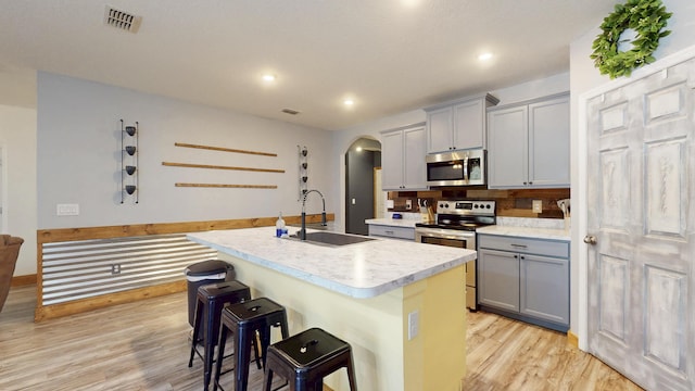 551 SW Lairo Ave, Port Saint Lucie, FL 34953 - kitchen with arched walkways, light wood-style flooring, stainless steel appliances, a sink, and gray cabinetry