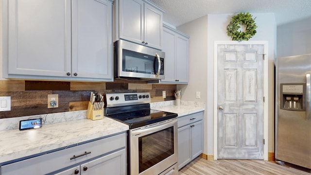 551 SW Lairo Ave, Port Saint Lucie, FL 34953 - kitchen with tasteful backsplash, stainless steel appliances, light countertops, light wood-type flooring, and gray cabinets
