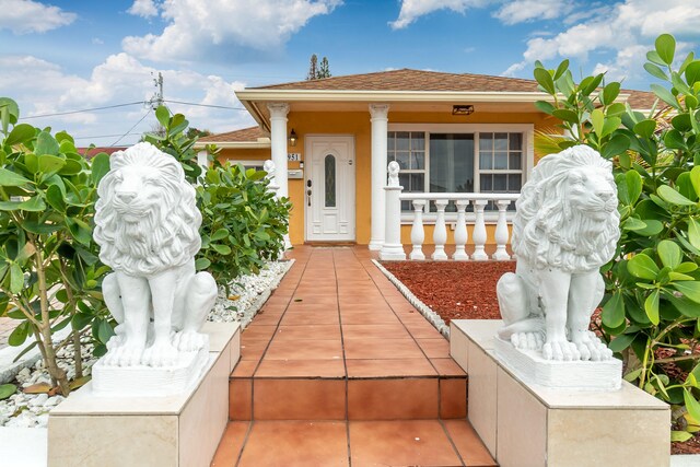 951 Green St, West Palm Beach, FL 33405 - doorway to property featuring covered porch, stucco siding, and roof with shingles