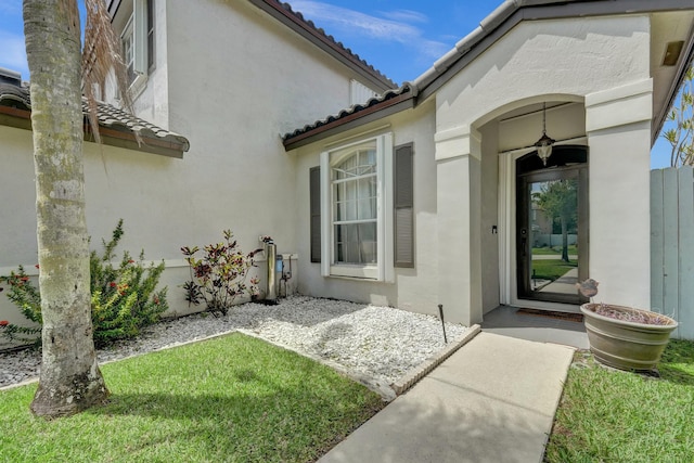 entrance to property with stucco siding, a lawn, and a tile roof
