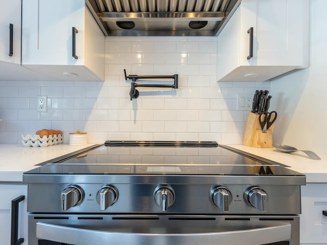 interior details with wall chimney range hood, white cabinets, light countertops, stainless steel range with electric cooktop, and backsplash