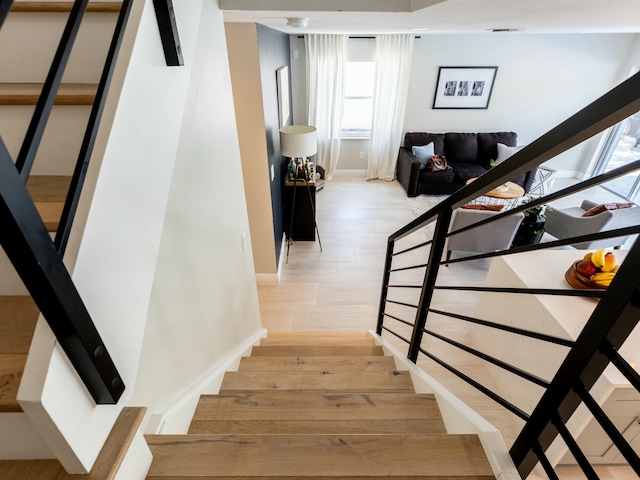 stairs featuring baseboards, wood finished floors, and a healthy amount of sunlight