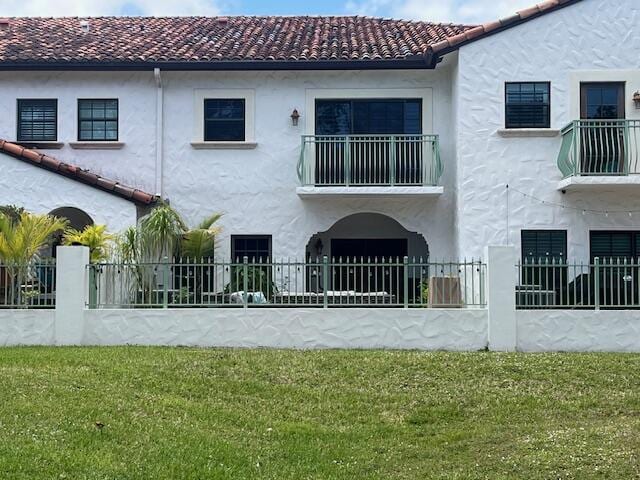 back of house featuring a tiled roof, a balcony, and fence private yard