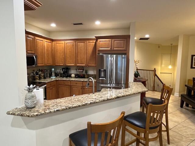 kitchen featuring stainless steel appliances, light tile patterned flooring, a breakfast bar area, light stone counters, and a peninsula