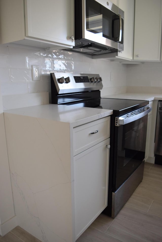kitchen featuring tasteful backsplash, light wood-style flooring, appliances with stainless steel finishes, light countertops, and white cabinetry