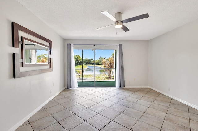 spare room with baseboards, a textured ceiling, a water view, a ceiling fan, and light tile patterned floors