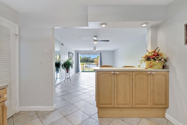 kitchen featuring a peninsula, light brown cabinetry, light tile patterned flooring, baseboards, and ceiling fan