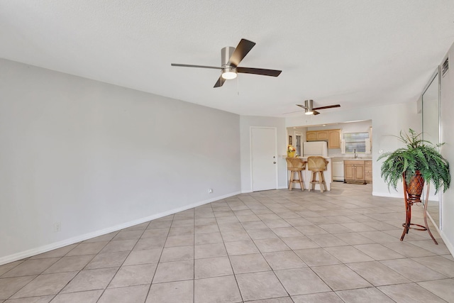 unfurnished living room featuring baseboards, light tile patterned flooring, ceiling fan, and a sink