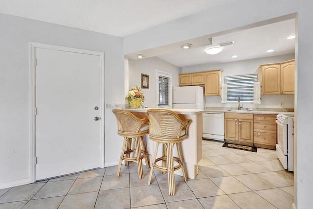 kitchen featuring light brown cabinets, white appliances, a kitchen bar, light countertops, and a sink