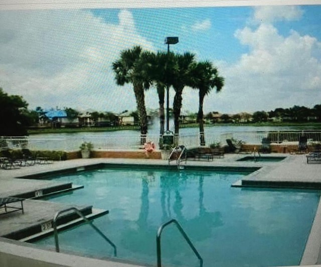 pool featuring fence, a water view, and a patio