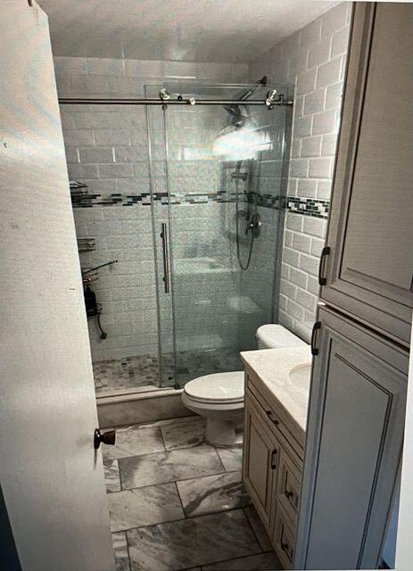 bathroom featuring toilet, a stall shower, marble finish floor, and vanity