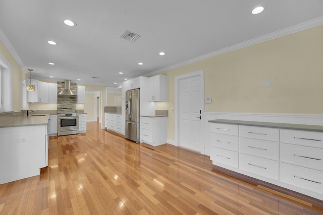 kitchen with wall chimney range hood, appliances with stainless steel finishes, white cabinetry, visible vents, and ornamental molding